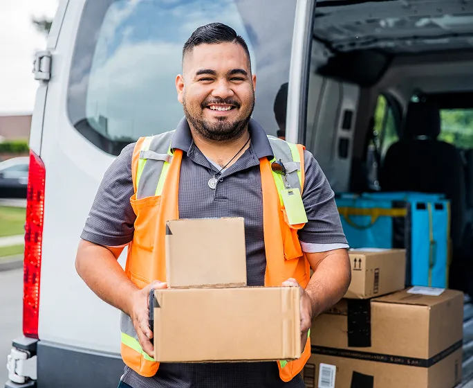 Smiling delivery worker holding parcels by a van